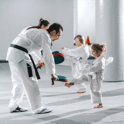 Small group of kids in doboks practicing with their trainers taekwondo moves while kicking in kick target.